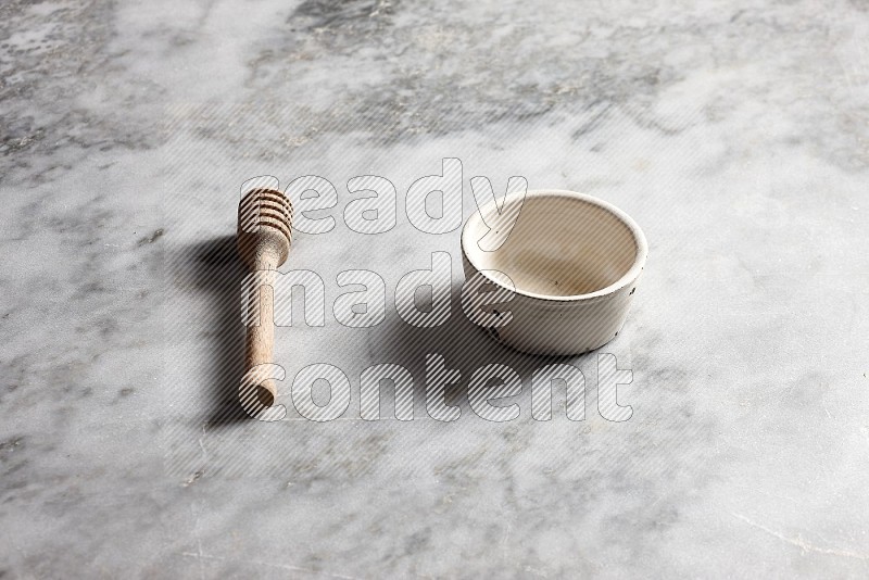 White Pottery Bowl with wooden honey handle on the side with grey marble flooring, 45 degree angle