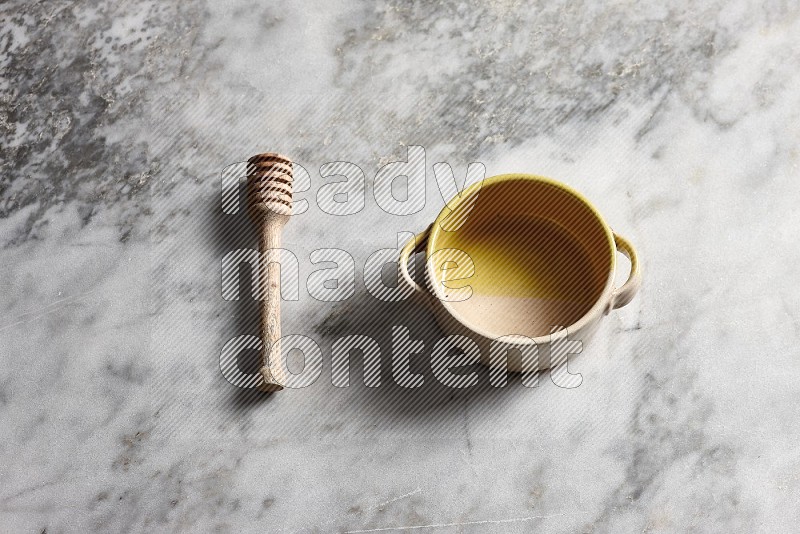 Multicolored Pottery bowl with wooden honey handle on the side with grey marble flooring, 65 degree angle