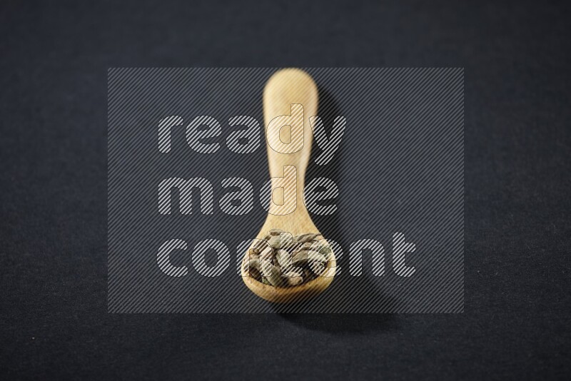 A wooden spoon full of cardamom on black flooring