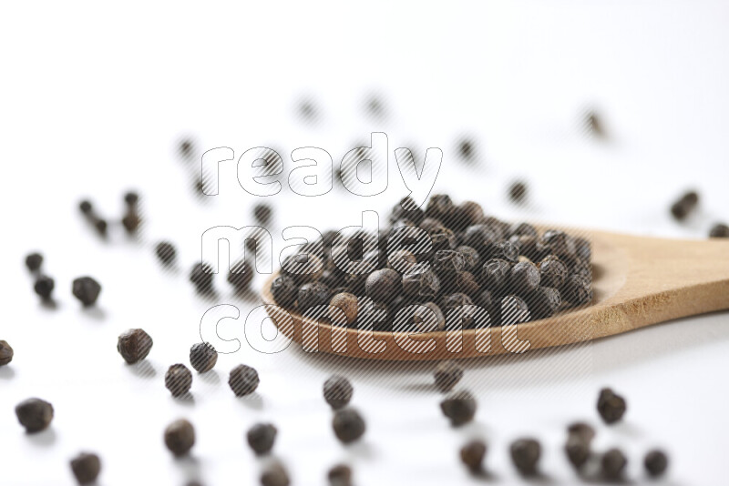 Black pepper beads with wooden spoon on white background