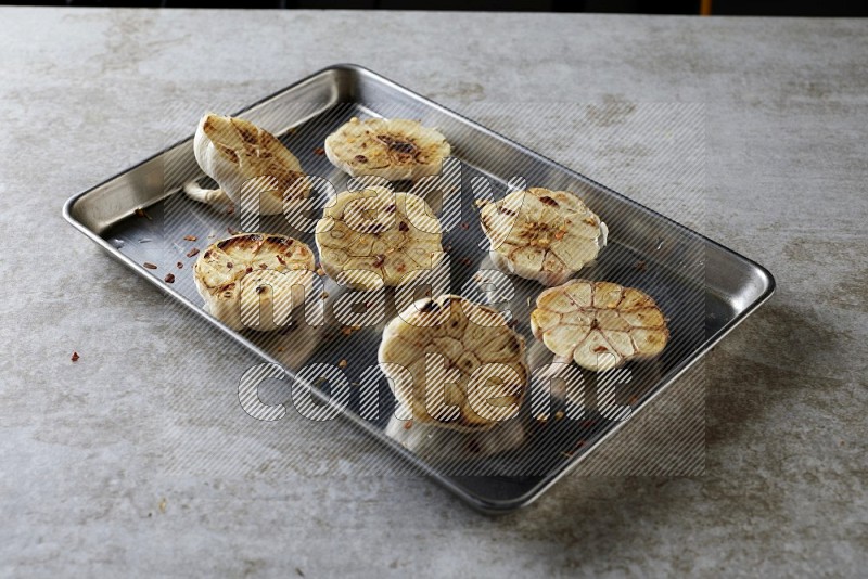 half's roasted garlic in a stainless tray on a grey textured countertop