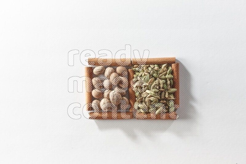 مربعان من أعواد القرفة ممتلئان بحبوب الهيل وجوزة الطيب علي خلفية بيضاء