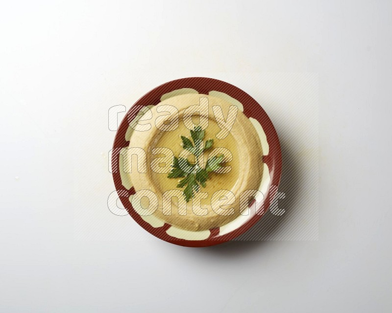 Hummus in a traditional plate garnished with parsley on a white background