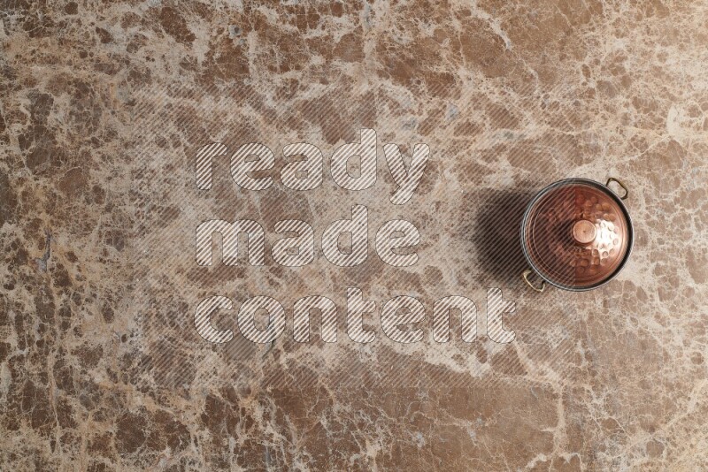 A small copper pot on beige marble background