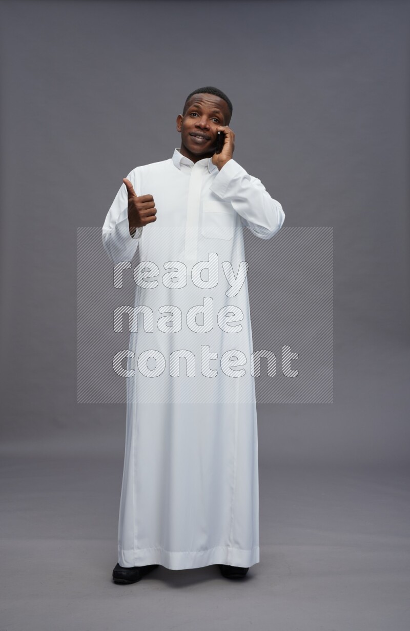 Saudi man wearing thob standing talking on phone on gray background