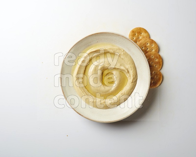 Hummus in a pottry plate garnished with olive oil on a white background