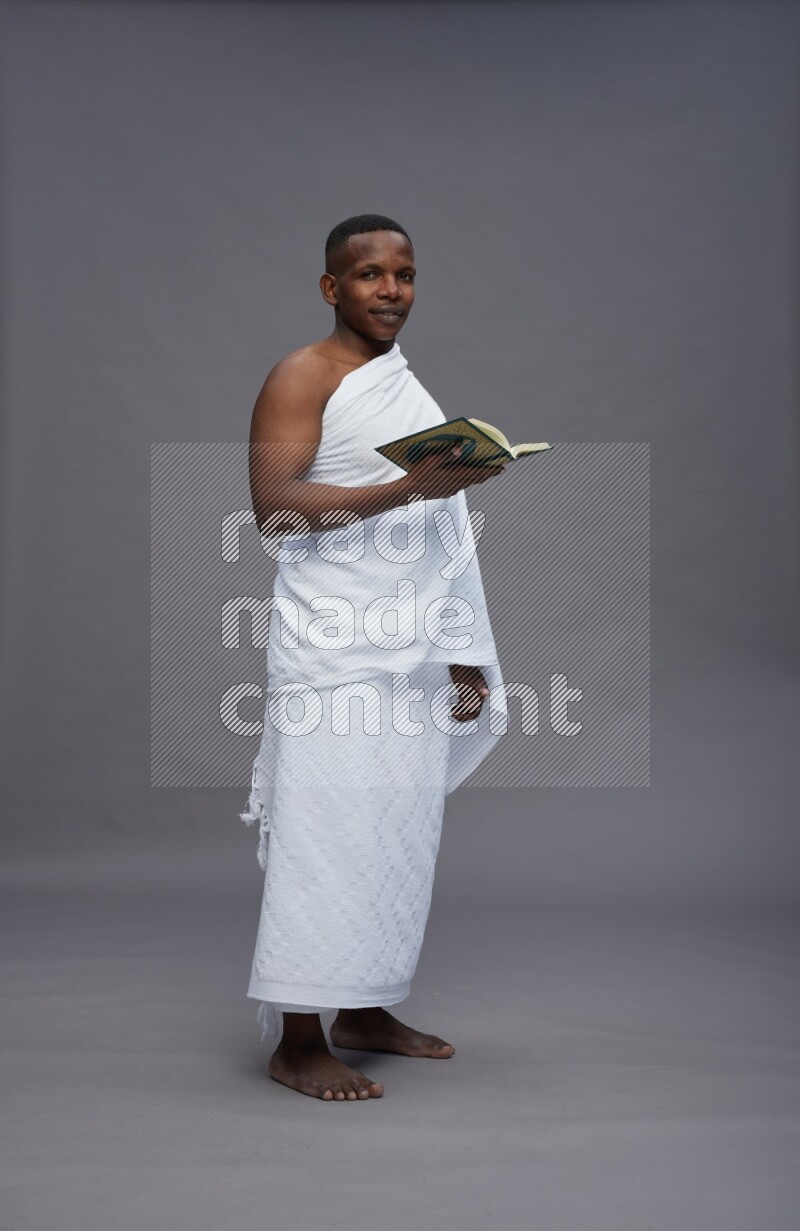 A man wearing Ehram Standing reading quran on gray background