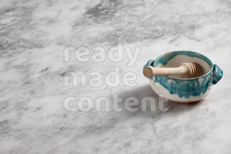 Multicolored pottery bowl with wooden honey dipper in it on grey marble background