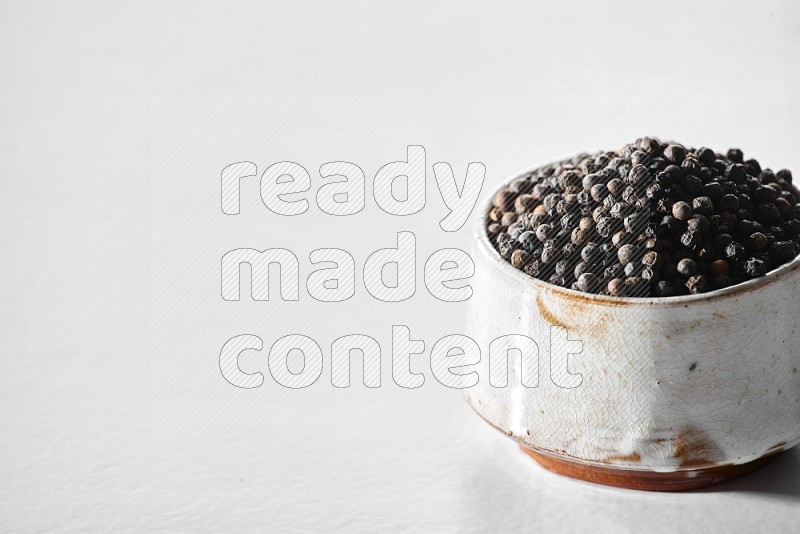 A white ceramic bowl full of black pepper on white flooring