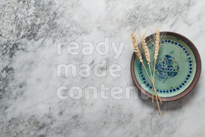 Wheat stalks on decorative pottery plate on grey marble background