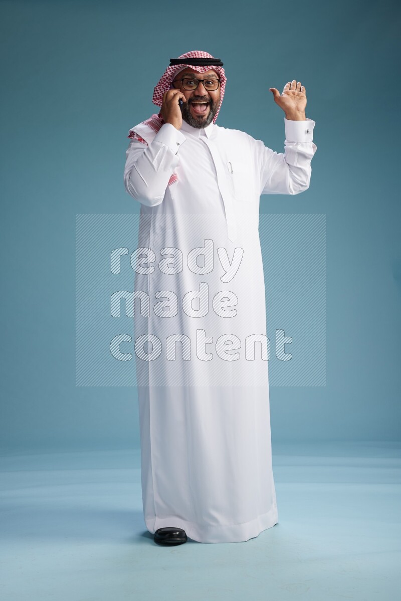Saudi Man with shimag Standing talking on phone on blue background