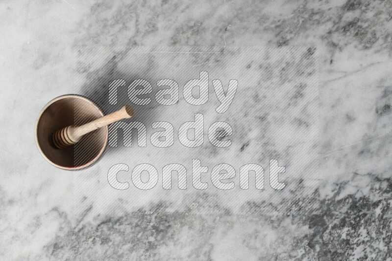 وعاء فخاري بيج مع ملعقة عسل خشبية بداخله على خلفية من الرخام الرمادي