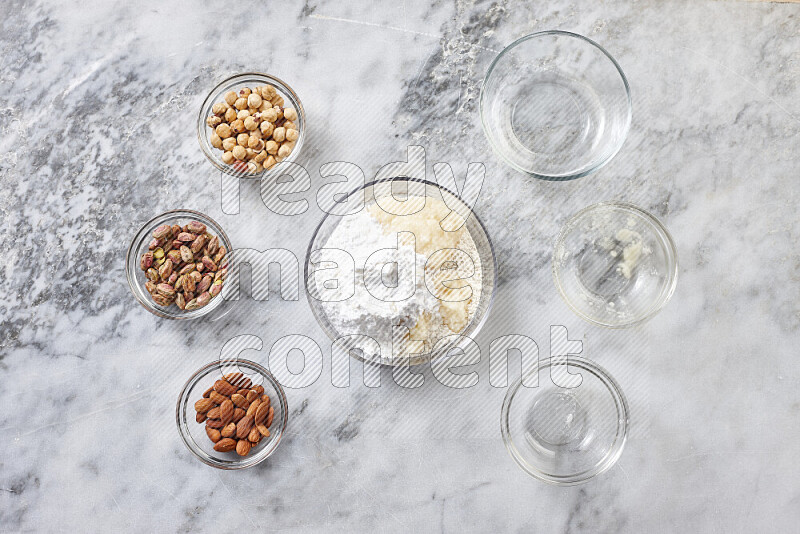 Ghoriba step by step with its ingredient, flour, powdered sugar, ghee and nuts on grey marble background