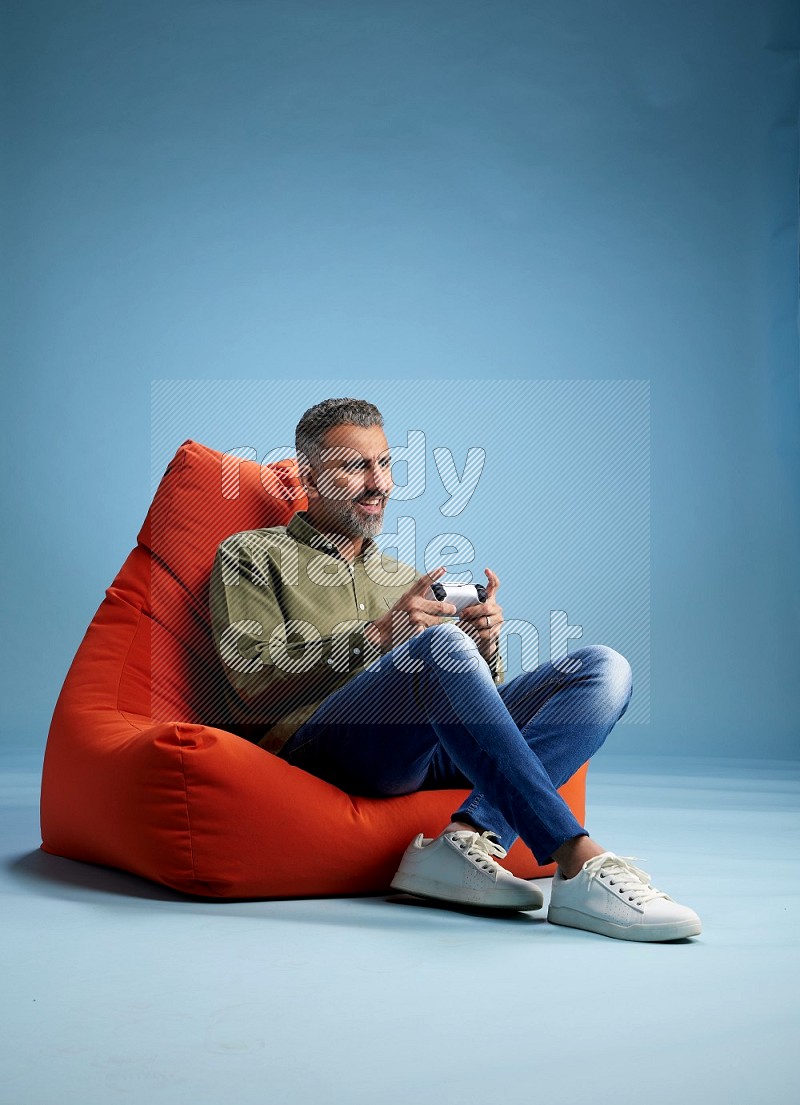 A man sitting on an orange beanbag and gaming with joystick