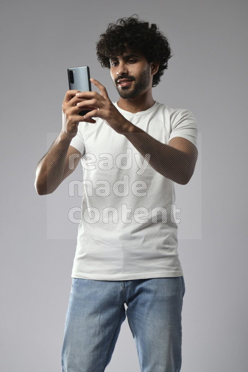 A man wearing casual standing and shooting with his phone on white background