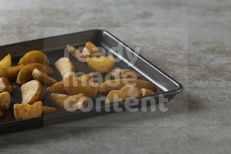 wedges potato in a black stainless steel rectangle tray on grey textured counter top