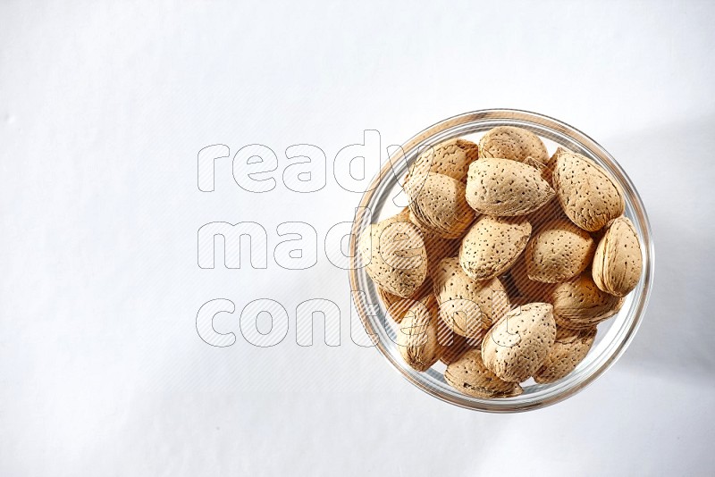 A glass bowl full of almonds on a white background in different angles