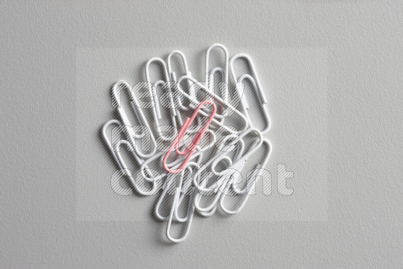 A pink paperclip surrounded by bunch of white paperclips on grey background