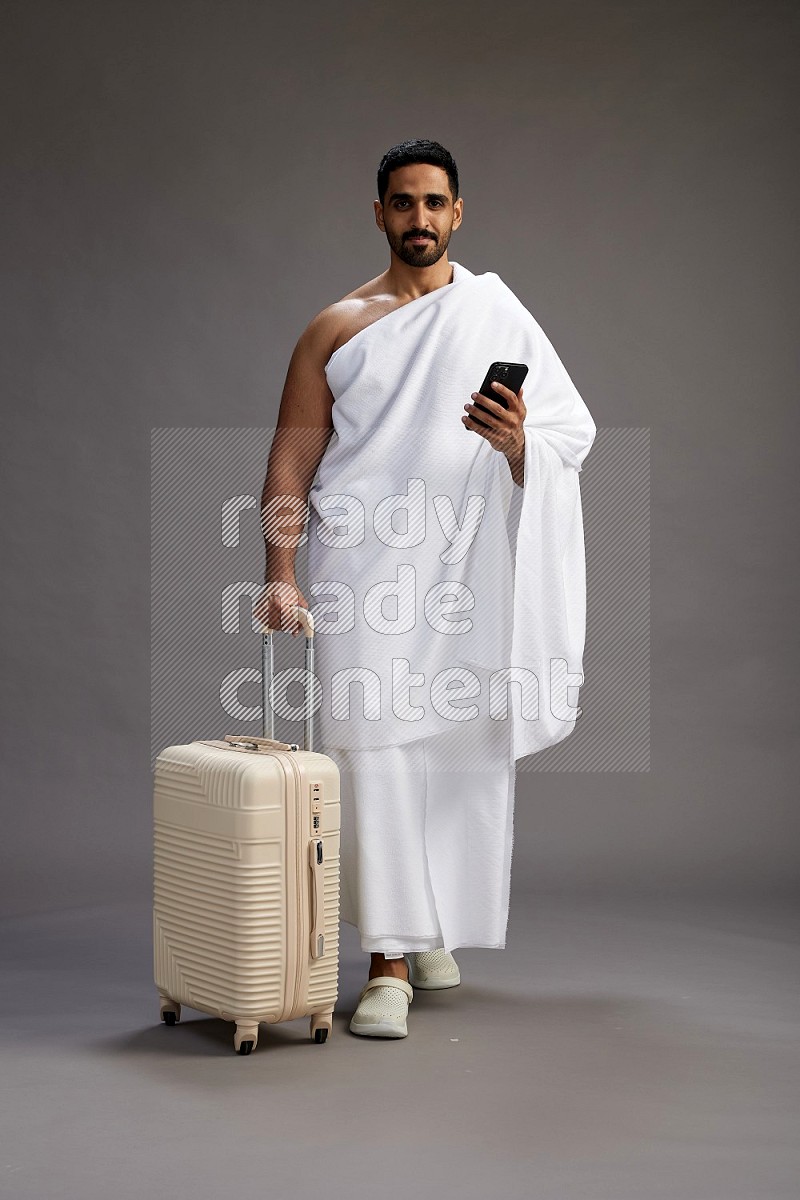 A man wearing Ehram Standing holding traveling bag on gray background