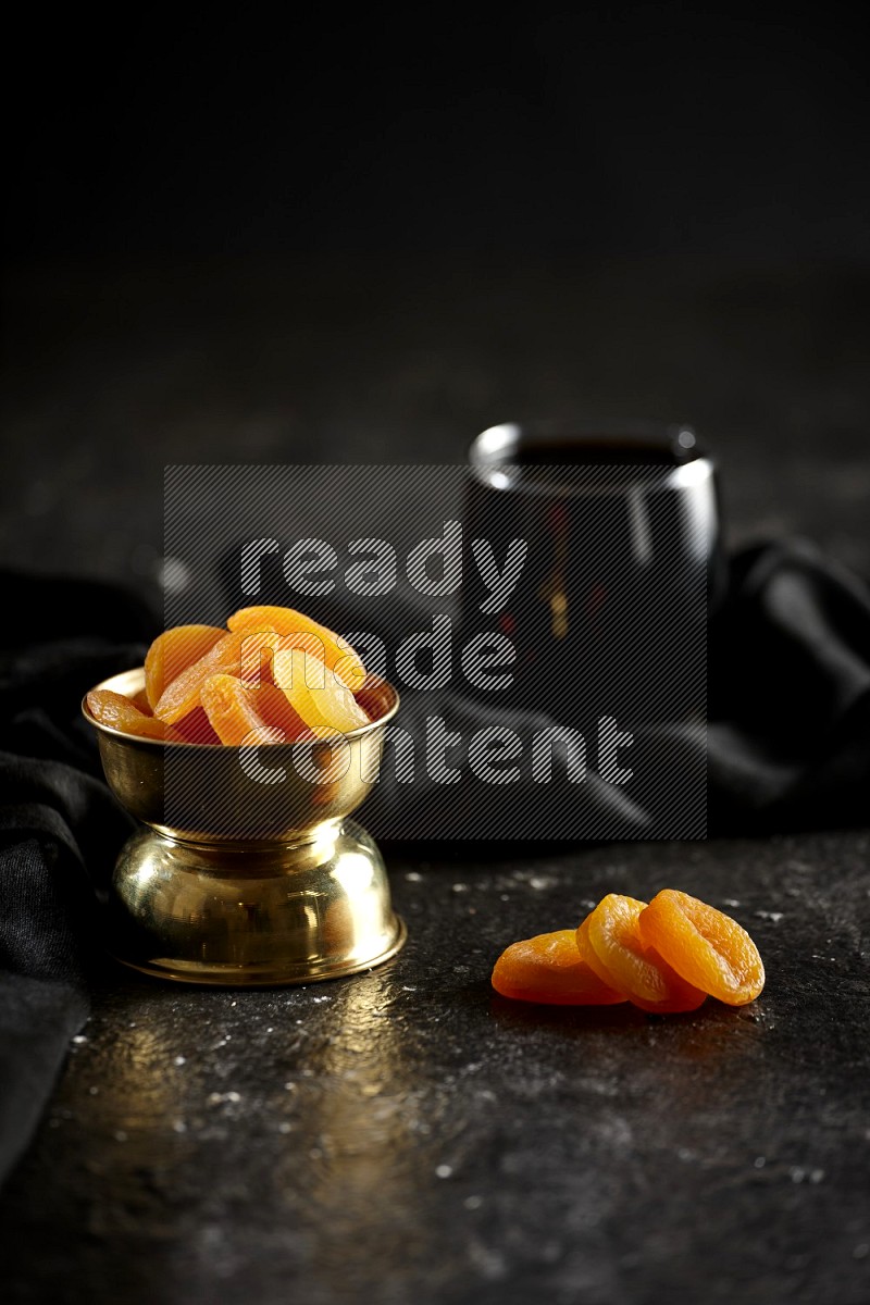 Dried fruits in a metal bowl with tamarind and a napkin in a dark setup