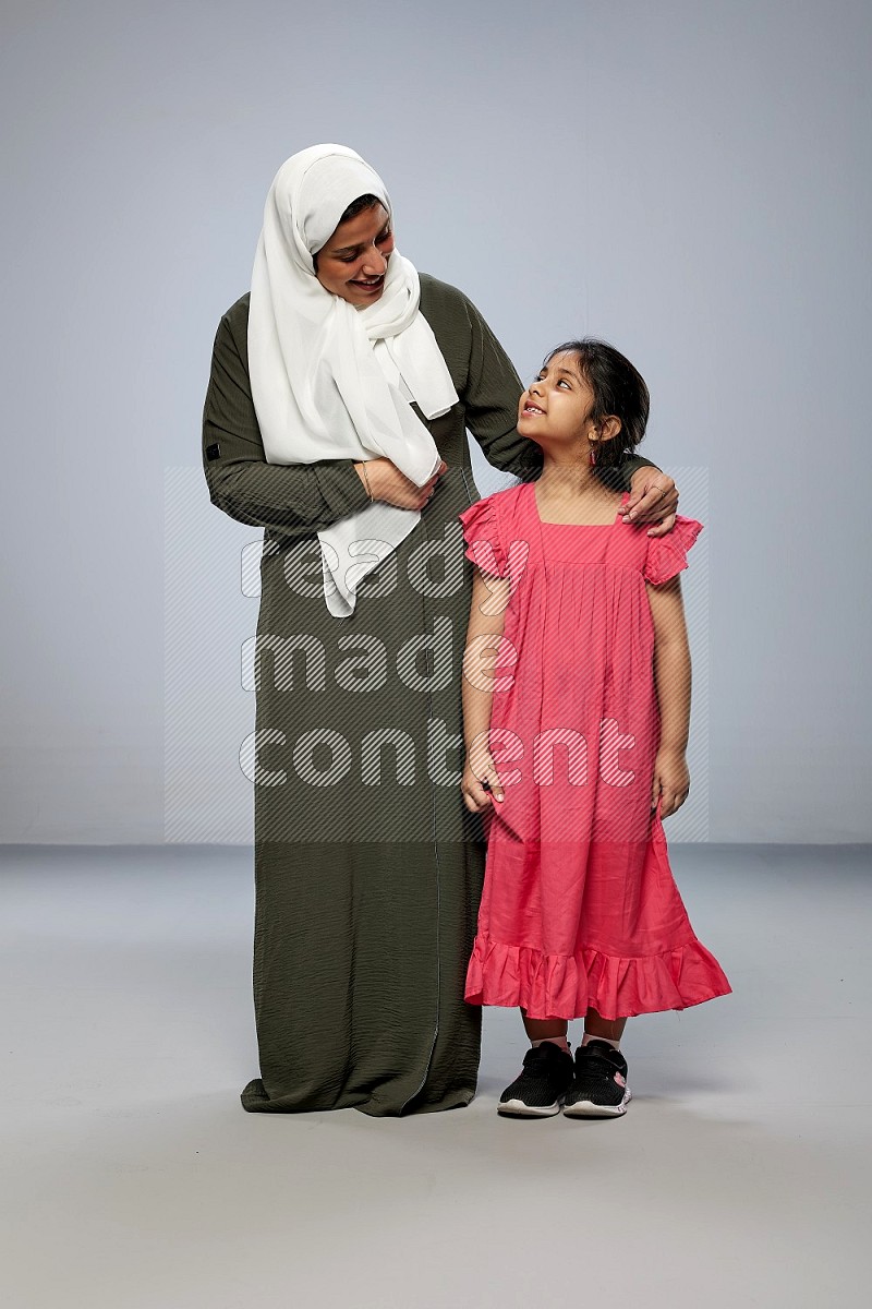 A girl and her mother interacting with the camera on gray background