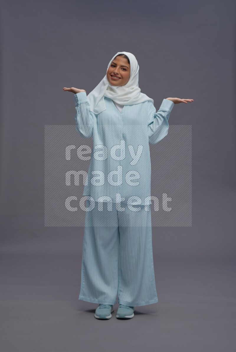 Saudi woman wearing hijab clothes standing interacting with the camera on gray background