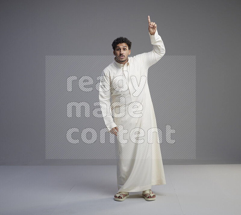 A Saudi man standing wearing thob interacting with the camera on gray background