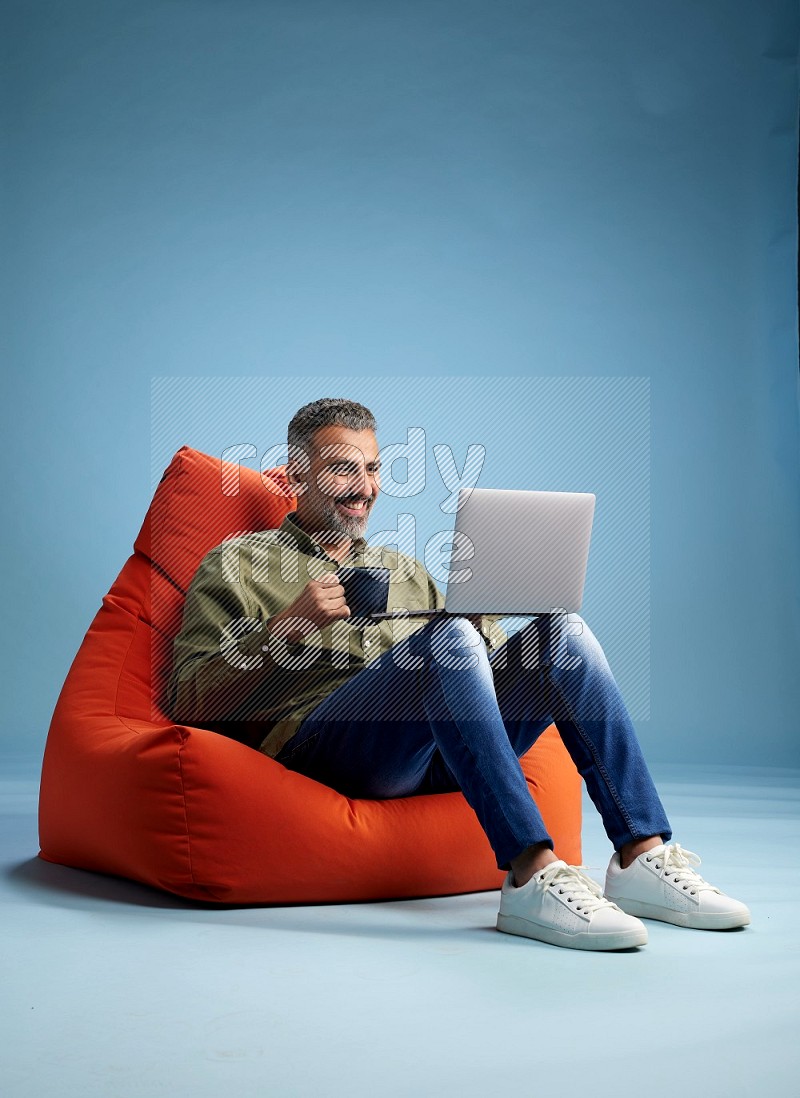 A man sitting on an orange beanbag and working on laptop