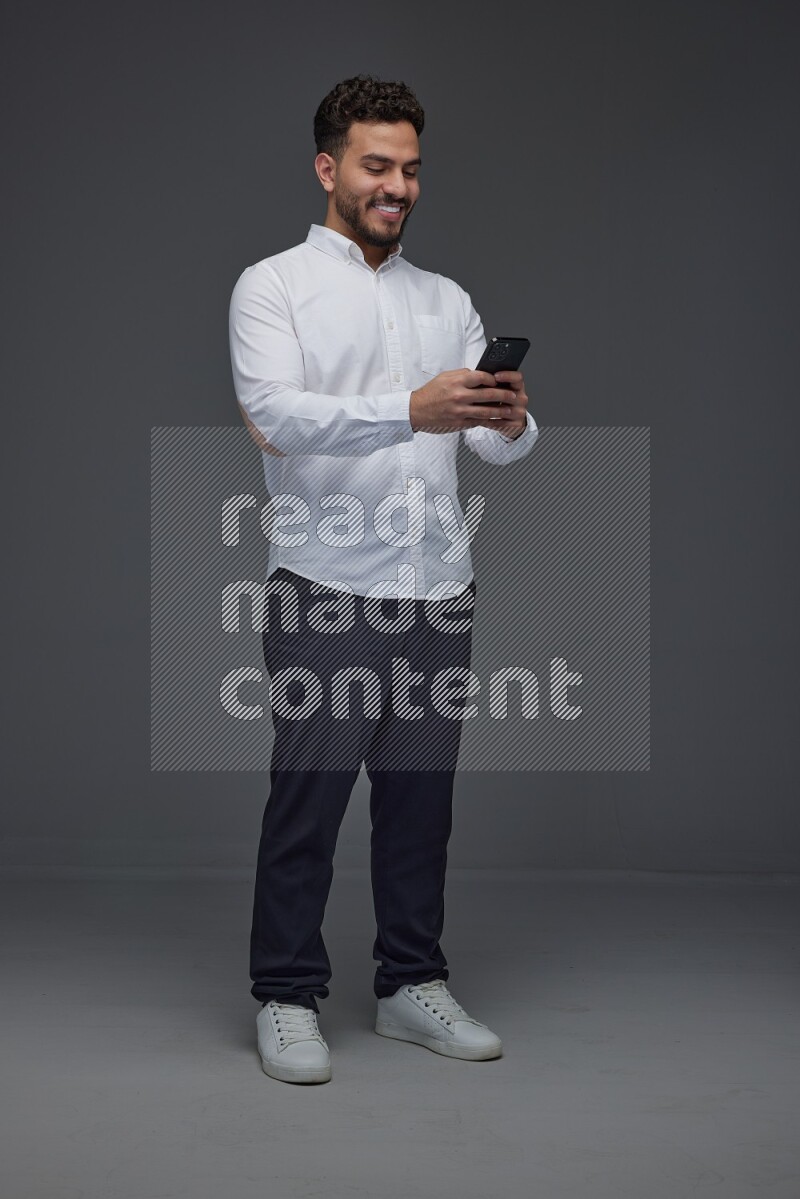 A man wearing smart casual standing and using his phone eye level on a gray background