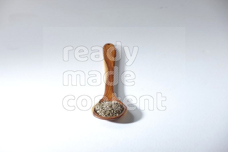 A wooden ladle full of cumin seeds on a white flooring