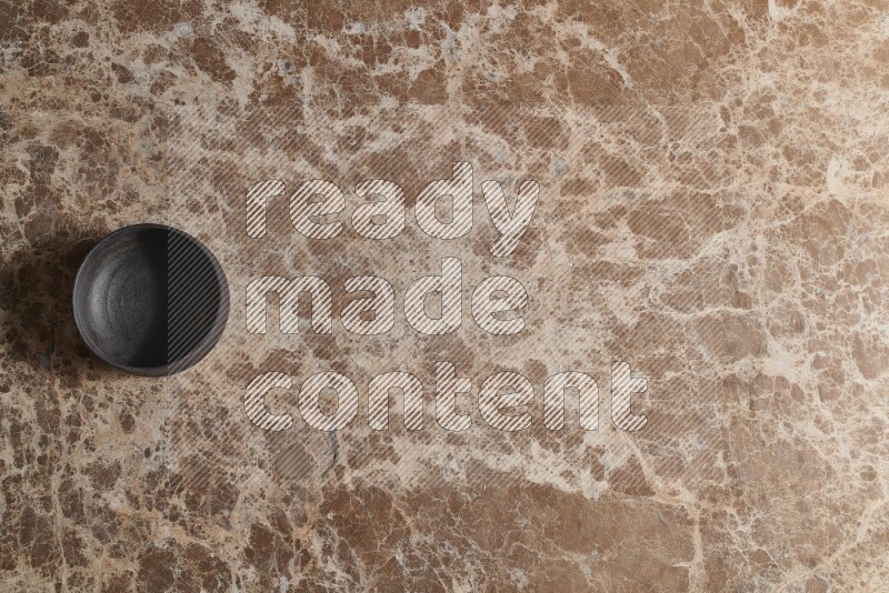 A black pottery bowl on beige marble background