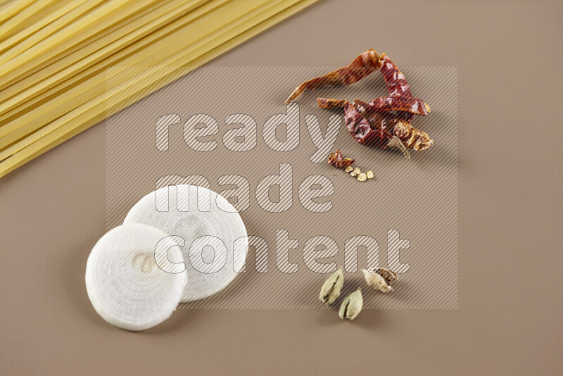 Raw pasta with different ingredients such as cherry tomatoes, garlic, onions, red chilis, black pepper, white pepper, bay laurel leaves, rosemary and cardamom on beige background