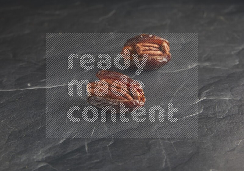 two pecan stuffed madjoul dates on a black textured background