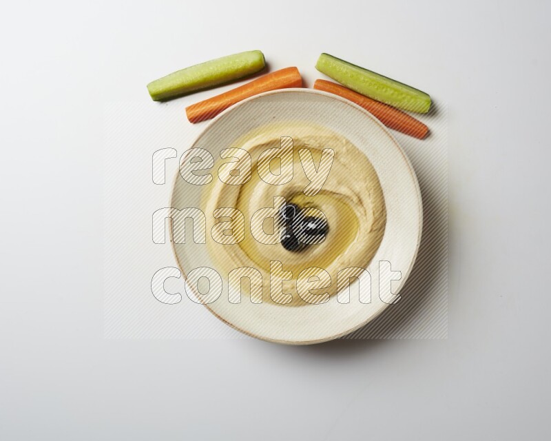 Hummus in a pottry plate garnished with black olives on a white background