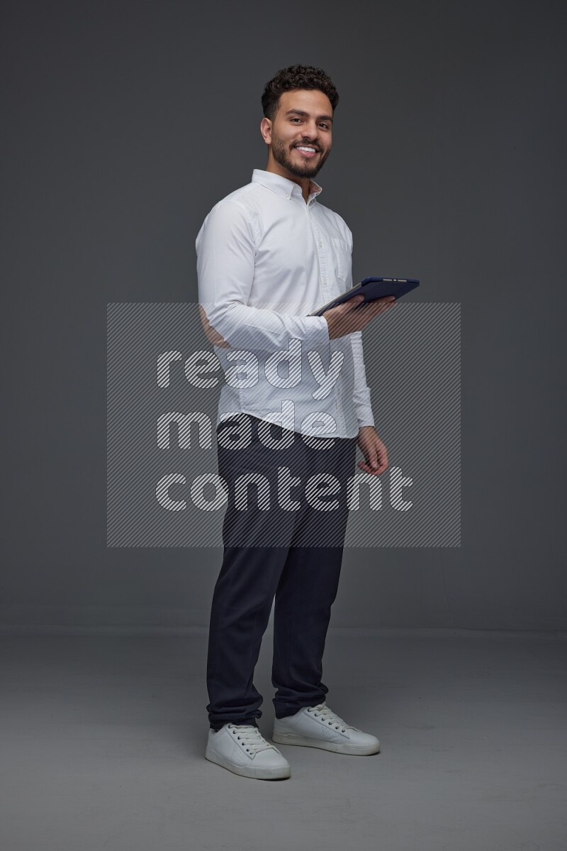 A man wearing smart casual standing and using his tablet eye level on a gray background
