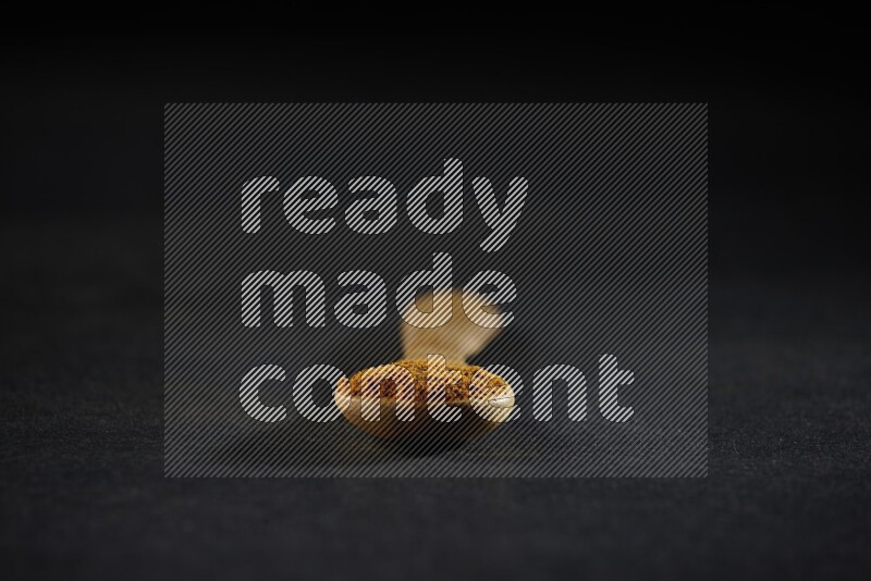 ملعقة خشبية ممتلئة ببودرة الكركم على خلفية سوداء