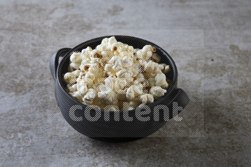 popcorn in a black handheld ceramic bowl on a grey textured countertop