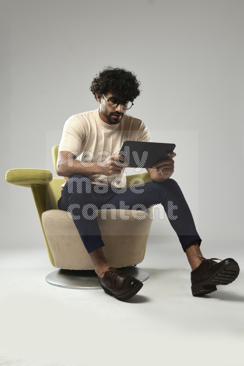 A man wearing casual sitting on a chair gaming on a tablet on white background