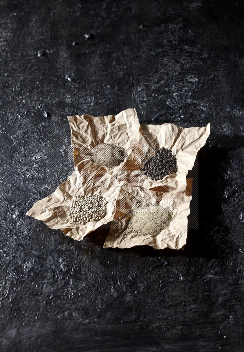 Crumpled pieces of paper full of black and white pepper beads and powder on a textured black flooring