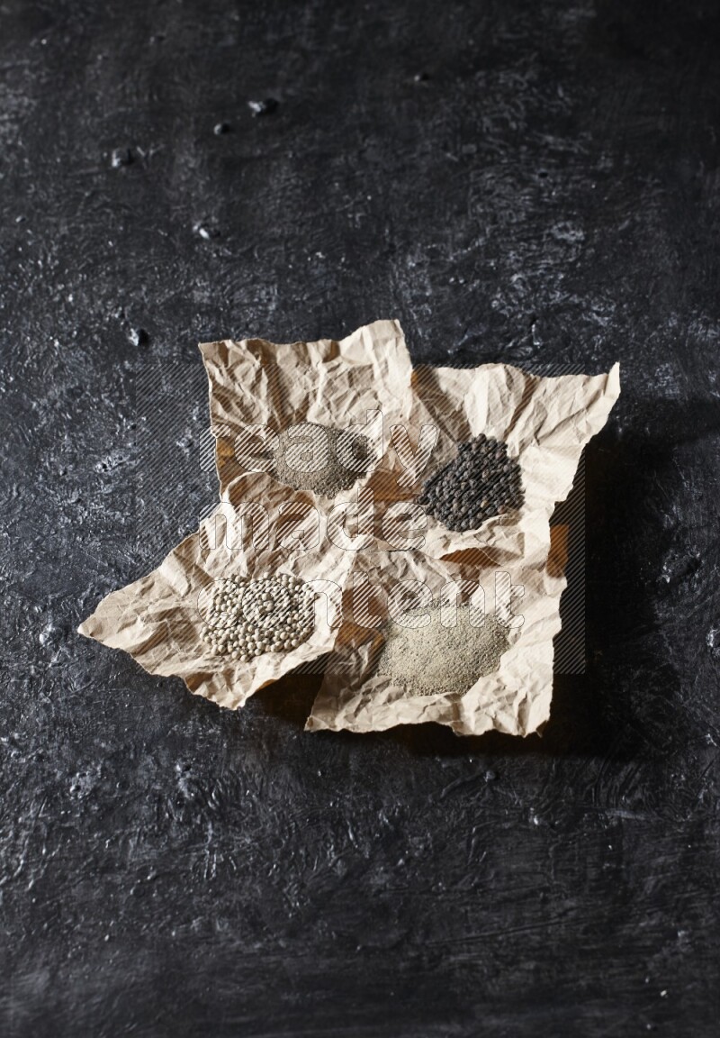 Crumpled pieces of paper full of black and white pepper beads and powder on a textured black flooring
