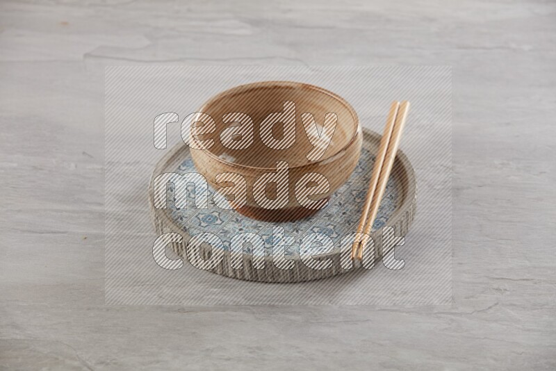 multi color pottery round bowl on top of multi color round ceramic plate and chopsticks, on grey textured countertop