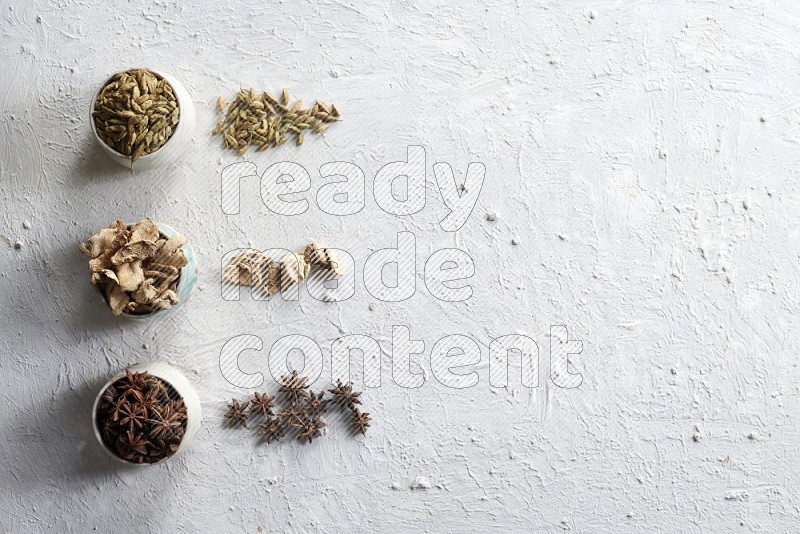 Cardamom, ginger and star anise in 3 bowls on a textured white background