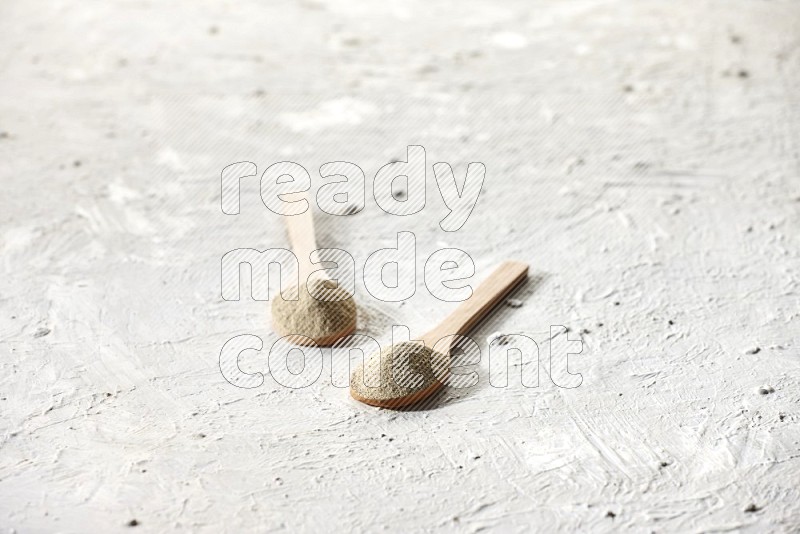 2 wooden spoons full of white pepper powder on textured white flooring