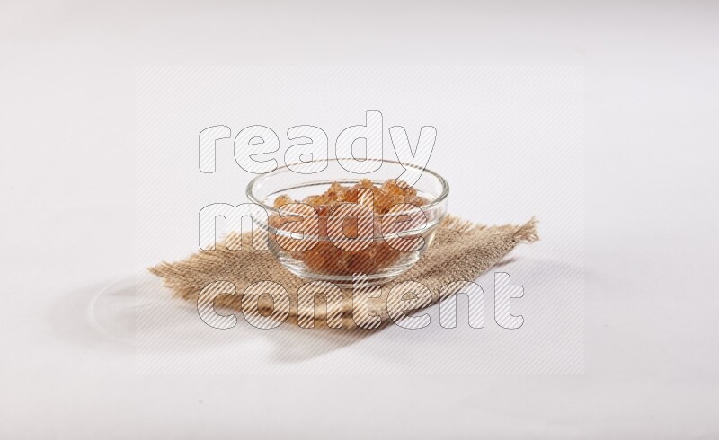 A glass bowl full of gum arabic on a burlap piece on white flooring