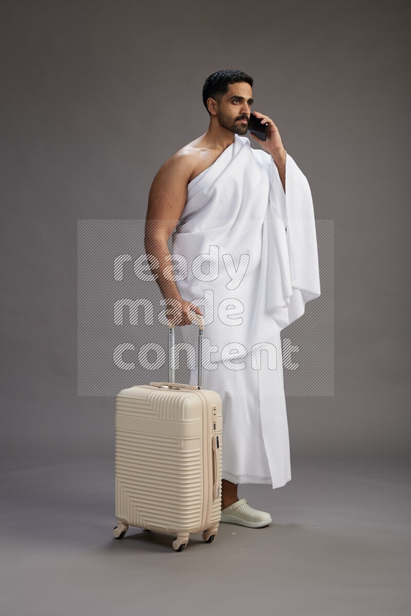 A man wearing Ehram Standing holding traveling bag on gray background
