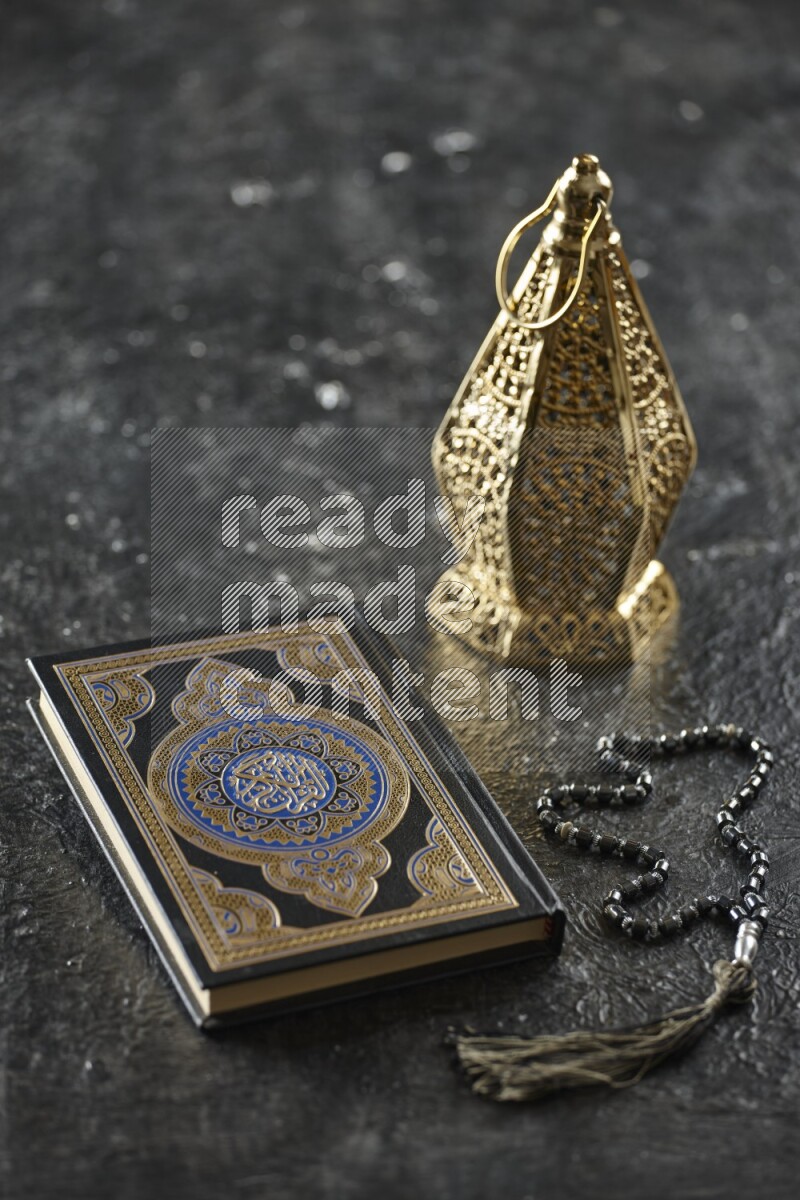 A golden lantern with different drinks, dates, nuts, prayer beads and quran on textured black background