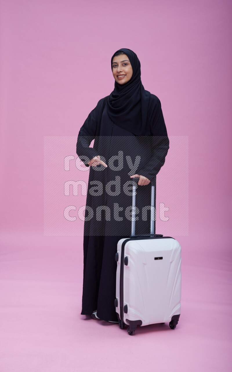 Saudi woman wearing Abaya standing holding bag on pink background