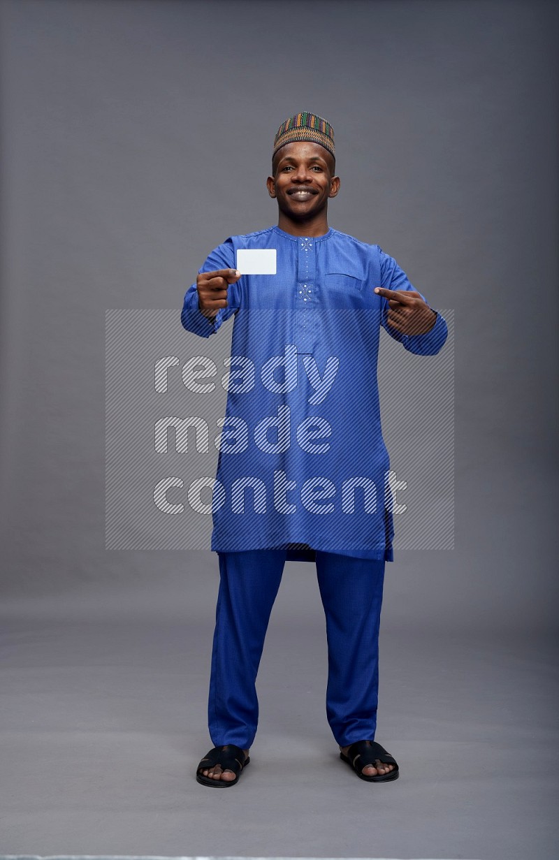 Man wearing Nigerian outfit standing holding ATM card on gray background