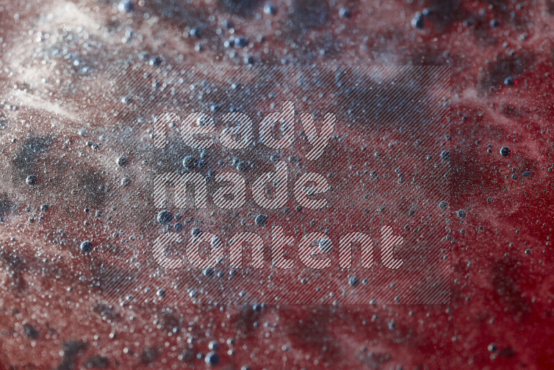 لقطات مقربة لقطرات ألوان مائية زرقاء على سطح الزيت على خلفية حمراء