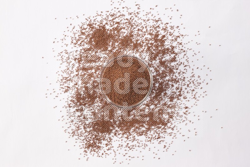 وعاء زجاجي ممتلئ ببذور حب الرشاد مع بعض البذور متناثرة على خلفية بيضاء